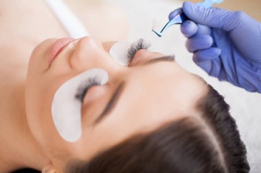 Kirpiklerini uzat. Sahte kirpikler. Kirpik uzatma prosedürü. Profesyonel stilist, kadın kirpiklerini uzatıyor. Usta ve bir müşteri güzellik salonunda.