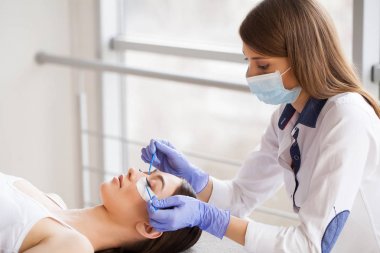 Kirpiklerini uzat. Sahte kirpikler. Kirpik uzatma prosedürü. Profesyonel stilist, kadın kirpiklerini uzatıyor. Usta ve bir müşteri güzellik salonunda.