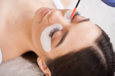 Kirpiklerini uzat. Sahte kirpikler. Kirpik uzatma prosedürü. Profesyonel stilist, kadın kirpiklerini uzatıyor. Usta ve bir müşteri güzellik salonunda.