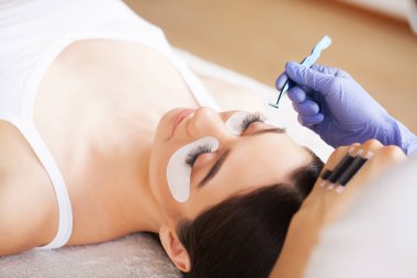 Kirpiklerini uzat. Sahte kirpikler. Kirpik uzatma prosedürü. Profesyonel stilist, kadın kirpiklerini uzatıyor. Usta ve bir müşteri güzellik salonunda.