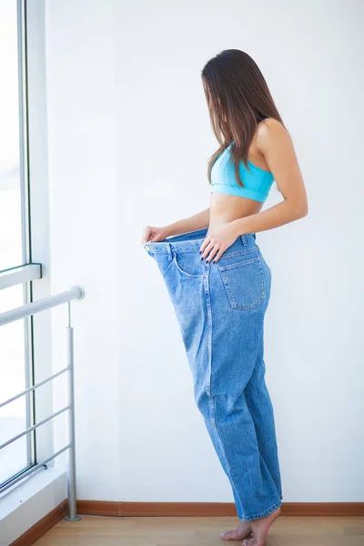 Dieta. Mulher mostra sua perda de peso e vestindo seus jeans velhos — Fotografia de Stock