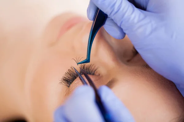 Extensiones de pestañas. Pestañas falsas. Procedimiento de extensión de pestañas. Estilista profesional que alarga las pestañas femeninas. Maestro y un cliente en un salón de belleza —  Fotos de Stock