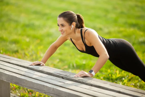 Mode de vie sain. Femme sportive faisant des exercices sur banc et écoutant de la musique en milieu urbain — Photo