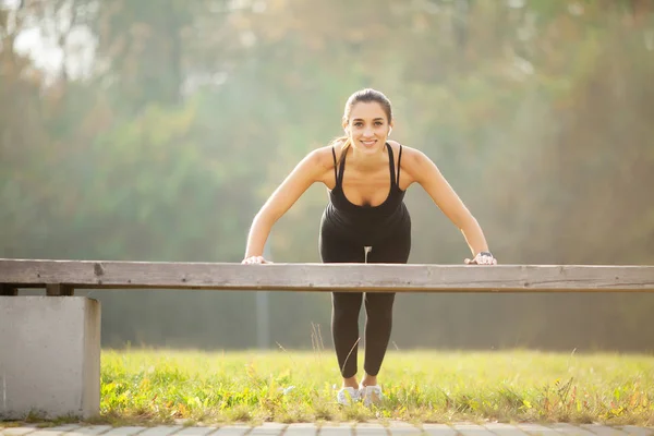Zdrowy styl życia. Kobieta sportowa robi ćwiczenia na ławce i słuchanie muzyki w środowisku miejskim — Zdjęcie stockowe