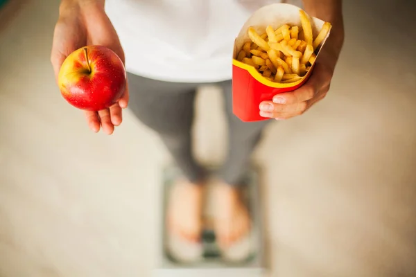 Régime alimentaire et saine alimentation. Jeune femme au choix entre les fruits et la malbouffe — Photo