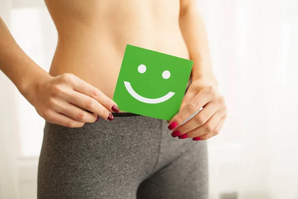 Women Health. Closeup Of Healthy Female With Beautiful Fit Slim Body In Black Panties Holding Green Card With Happy Smiley Face In Hands. Stomach Health And Good Digestion Concepts. High Resolution