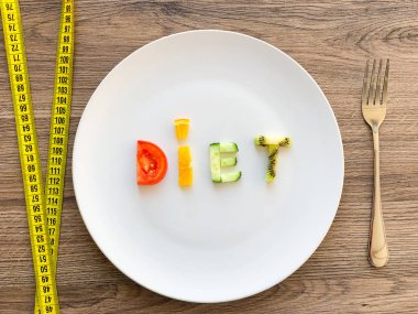 Kelime diyeti tabakta dilimlenmiş sebzelerden yapılır ve ahşap arka planda ölçülür.