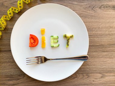 Kelime diyeti tabakta dilimlenmiş sebzelerden yapılır ve ahşap arka planda ölçülür.