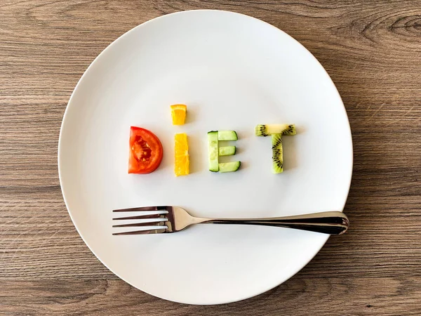 Word DIET made of sliced vegetables in plate with measuring on wood background — Stock Photo, Image