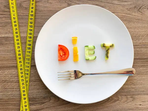 Word DIET made of sliced vegetables in plate with measuring on wood background — Stock Photo, Image