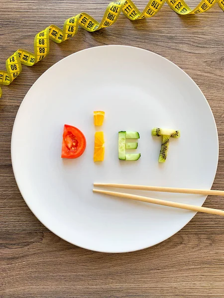 Word DIET made of sliced vegetables in plate with measuring on wood background — Stock Photo, Image