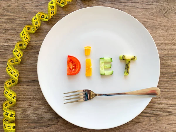 Word DIET made of sliced vegetables in plate with measuring on wood background — Stock Photo, Image