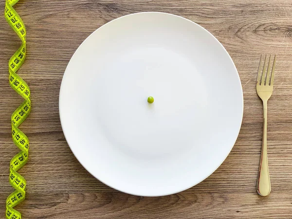 Kost. Lider av anorexi. Beskäras bild Pea på vit plåt, med gaffel och mätning — Stockfoto