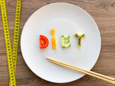 Kelime diyeti tabakta dilimlenmiş sebzelerden yapılır ve ahşap arka planda ölçülür.