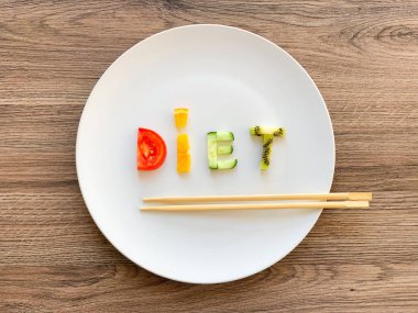 Tahta arka planda beyaz tabakta dilimlenmiş sebzelerden yapılan diyet.