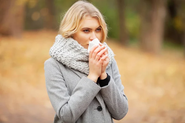 Rapariga a espirrar em tecido. Uma jovem a assoar o nariz no parque. Mulher retrato ao ar livre espirros porque frio e gripe — Fotografia de Stock