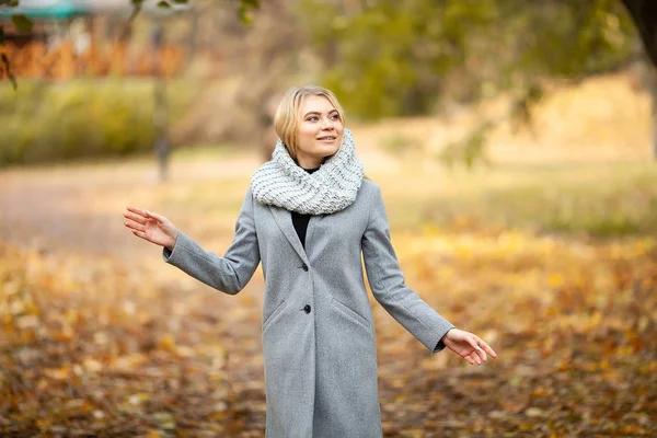 Erkältung und Grippe. junge Frau im grauen Mantel spaziert durch den Herbstpark und wärmt gefrorene Hand — Stockfoto