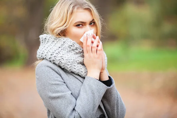 Chica estornudando en tejido. Una joven sonándose la nariz en el parque. Mujer retrato al aire libre estornudos porque el frío y la gripe — Foto de Stock