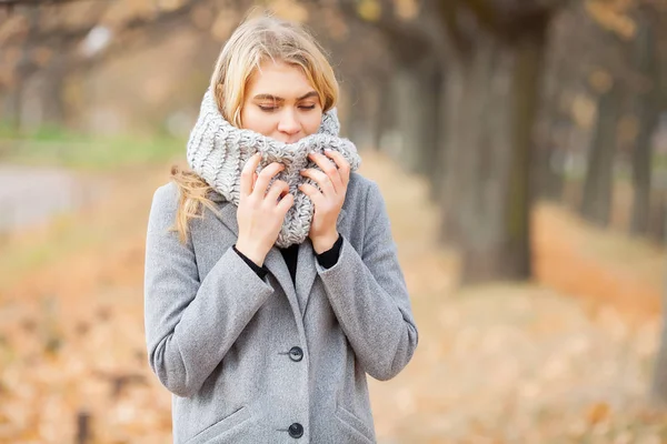 Холодно и грипп. Молодая женщина в сером пальто гуляет по осеннему парку и согревает замерзшую руку — стоковое фото