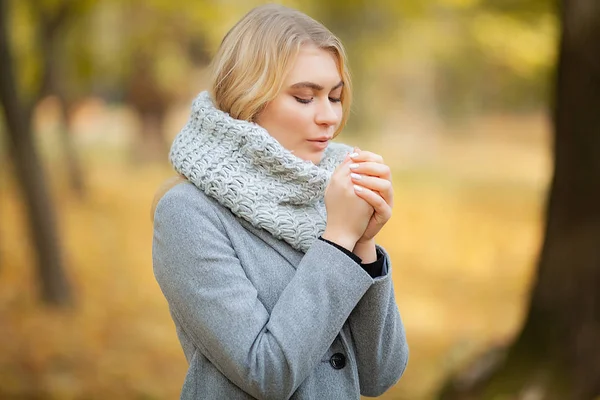 Resfriado y gripe. Mujer joven en un abrigo gris caminando en el parque de otoño y calienta la mano congelada — Foto de Stock