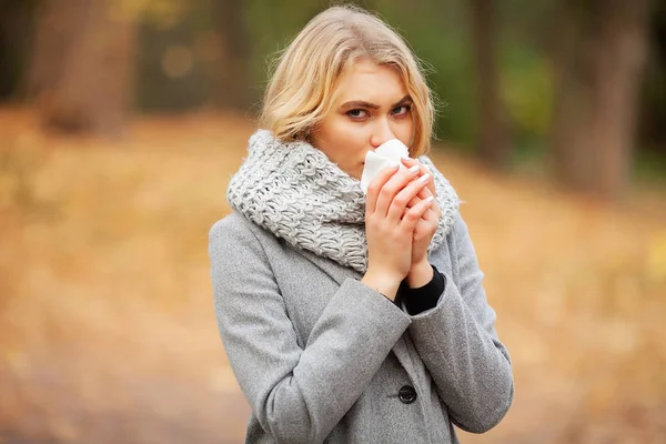 Chica estornudando en tejido. Una joven sonándose la nariz en el parque. Mujer retrato al aire libre estornudos porque el frío y la gripe — Foto de Stock