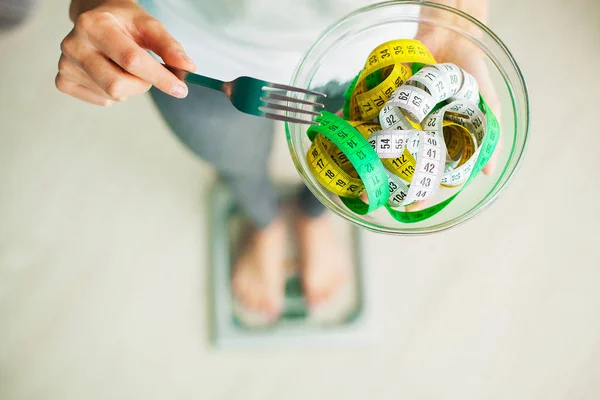 Diet and Weight Loss. Woman holds bowl and fork with measuring tape
