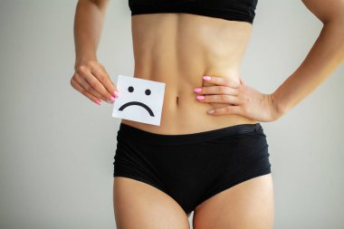 Kadın sağlığı. Kadın vücudu mide yakınındaki üzgün Smiley kartı tutan