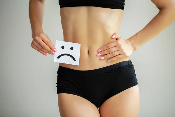 Salud de la mujer. Cuerpo femenino sosteniendo triste tarjeta sonriente cerca del estómago — Foto de Stock