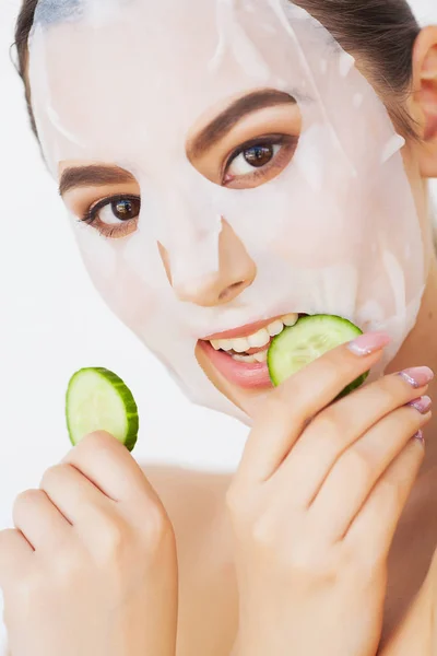 Beautiful young woman is getting facial clay mask at spa, lying with cucumbers on eyes — Stock Photo, Image