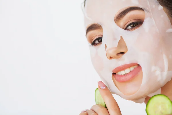 Beautiful young woman is getting facial clay mask at spa, lying with cucumbers on eyes — Stock Photo, Image