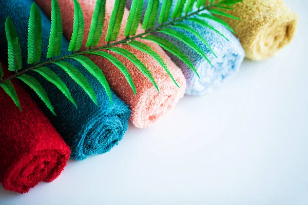 Toallas de colores y hojas de helecho en mesa blanca con espacio para copiar en el fondo de la sala de baño . — Foto de Stock