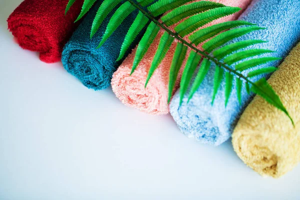 Toallas de colores y hojas de helecho en mesa blanca con espacio para copiar en el fondo de la sala de baño . — Foto de Stock