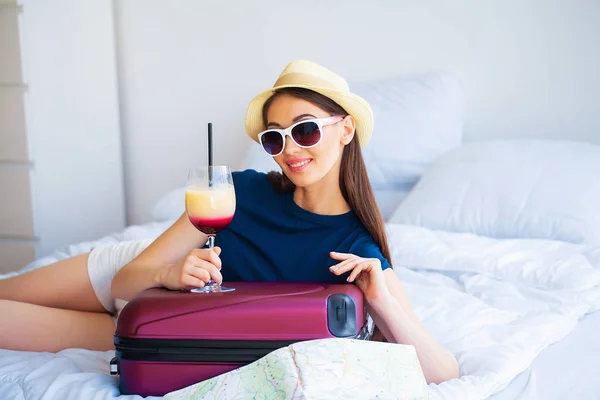 Piękny kobieta z koktajl i walizka na łóżko w hootel Pokój — Zdjęcie stockowe