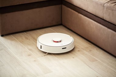 Akıllı Ev. Elektrikli süpürge robotu oturma odasında ahşap zeminde koşar..