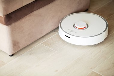 Akıllı Ev. Elektrikli süpürge robotu oturma odasında ahşap zeminde koşar..