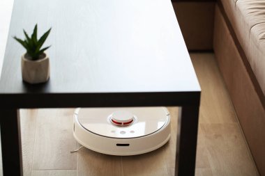 Akıllı Ev. Elektrikli süpürge robotu oturma odasında ahşap zeminde koşar..