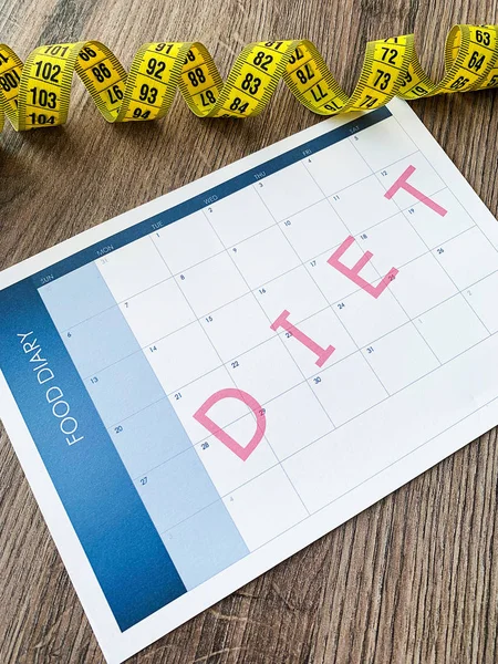 Diet plan concept. Measuring tape and diet plan on wooden background.