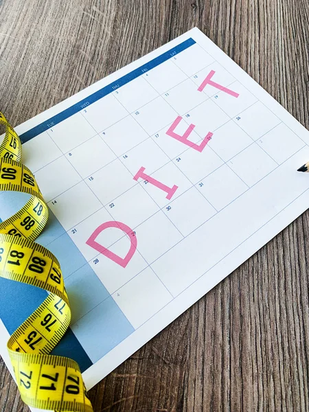 Diet plan concept. Measuring tape and diet plan on wooden background.