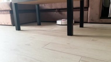 Akıllı Ev. Elektrikli süpürge robotu oturma odasında ahşap zeminde koşar.