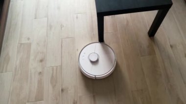 Akıllı Ev. Elektrikli süpürge robotu oturma odasında ahşap zeminde koşar.