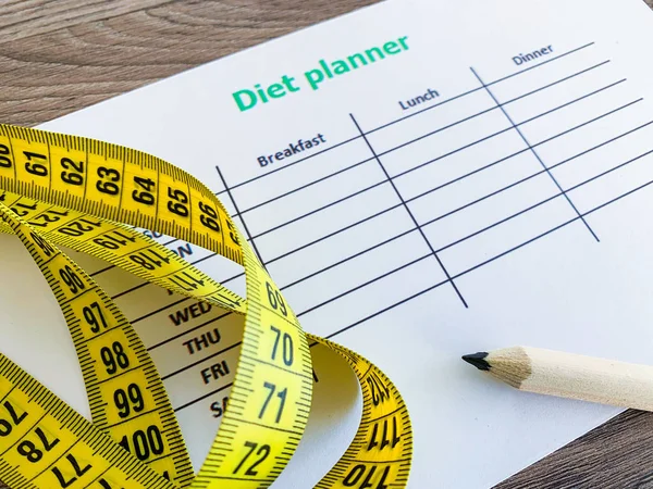 Diet plan concept. Measuring tape and diet plan on wooden background