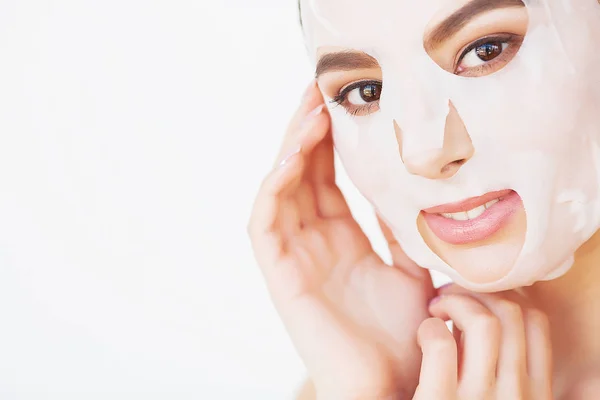 Hermosa joven mujer está recibiendo máscara de arcilla facial en el spa, acostado con pepinos en los ojos — Foto de Stock