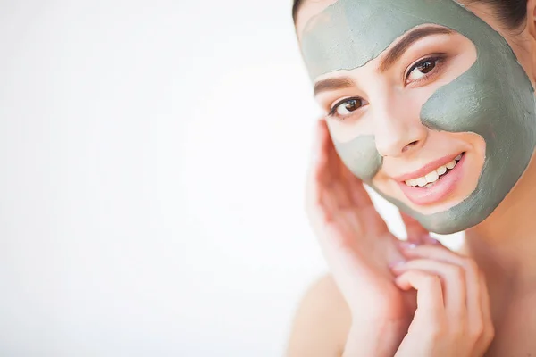 Cuidado de la piel. Mujer joven con máscara de arcilla cosmética sosteniendo pepino en su baño — Foto de Stock