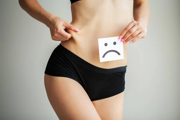 Salud de la mujer. Cuerpo femenino sosteniendo triste tarjeta sonriente cerca del estómago — Foto de Stock