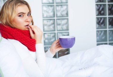 Yüksek sıcaklık. Genç kadın elinde tutarak ve yatakta yatarken termometre bakıyor