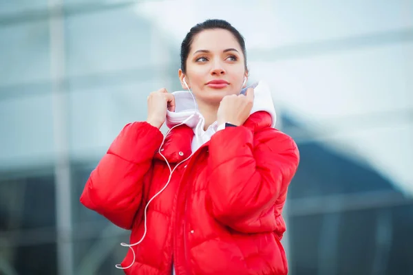 Фото 30-летней женщины в спортивной одежде, трогающей наушник Bluetooth и держащей мобильный телефон во время отдыха в Грин-Парке — стоковое фото