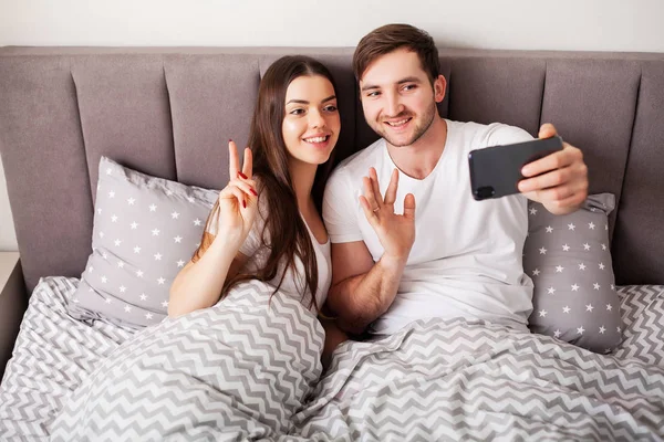 Sonriente joven pareja tomando selfie juntos en dormitorio — Foto de Stock