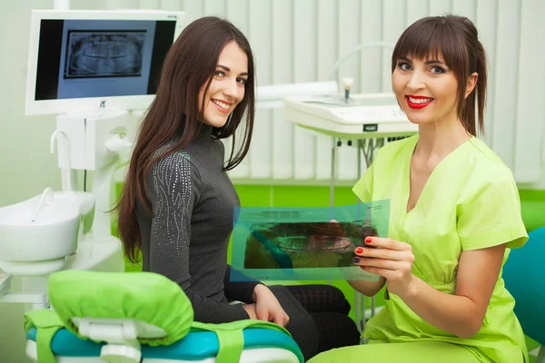 Dentista en el consultorio dental hablando con la paciente femenina y preparándose para el tratamiento —  Fotos de Stock