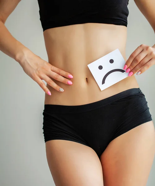 Woman Health Problem. Closeup Of Female With Fit Slim Body In Panties Holding White Card With Sad Smiley Face Near Her Stomach. Digestive Disorders, Period Pain, Health Issues Concept