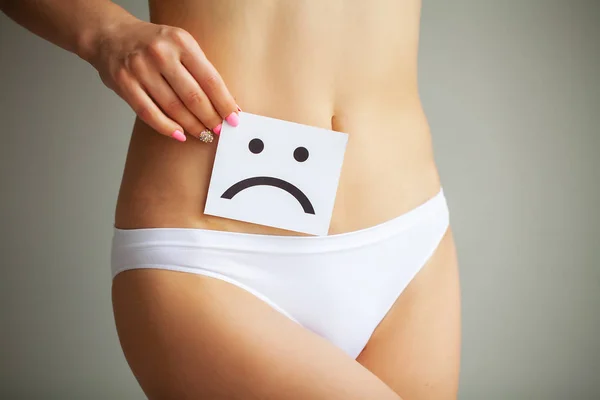 Woman Health Problem. Closeup Of Female With Fit Slim Body In Panties Holding White Card With Sad Smiley Face Near Her Stomach. Digestive Disorders, Period Pain, Health Issues Concept